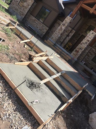 Concrete steps under construction in front of a stone house, with exposed wooden forms and gravel.