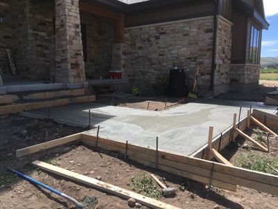 Concrete patio under construction beside a stone house, with wooden forms and rebar in the foreground.