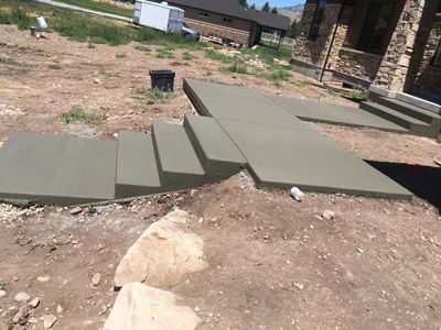 Concrete steps and ramps in a dirt yard, connecting uneven ground beside a stone house.