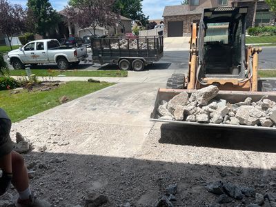 Construction equipment moving rocks onto a driveway in a residential area