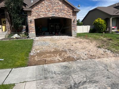 Suburban house with open garage and a muddy, torn-up driveway under repair
