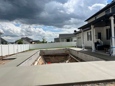 Backyard with a large rectangular in-ground pool under construction beside a house and cloudy sky
