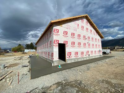 Partially built house wrapped in white insulation, with a concrete foundation under a cloudy sky.