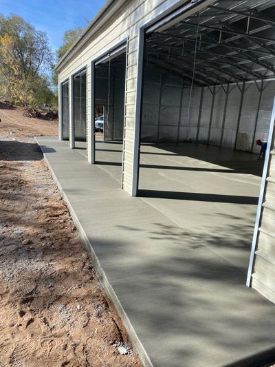 Empty concrete garage bays under construction with open steel framing and dirt beside the slab