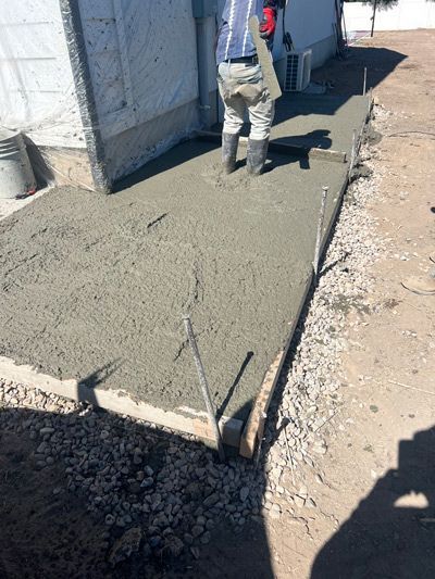 Fresh concrete sidewalk beside a white building, with a worker standing ahead.