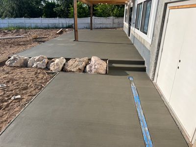 Concrete patio ramp beside a building, with rocks edging the path and a covered porch area.