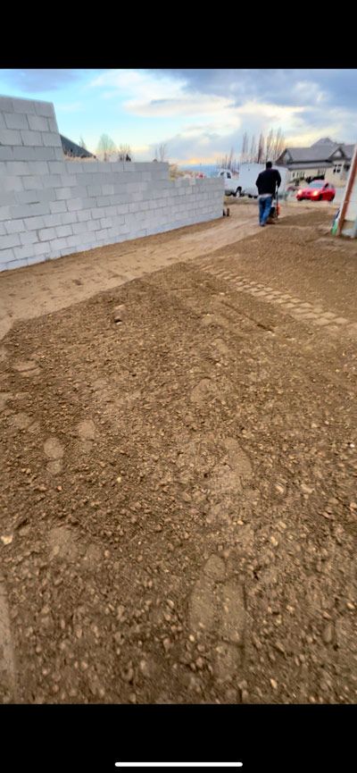 Dirt lot beside a cinderblock wall, with two people near a gate under a cloudy sky.