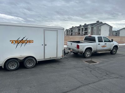 White pickup truck towing a white enclosed trailer in a parking lot under cloudy skies