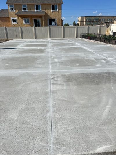 Freshly sealed gray concrete driveway in a suburban backyard, with a fence and houses in the background