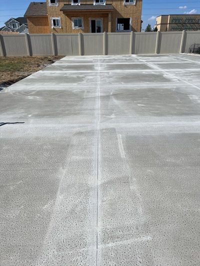 Concrete slab foundation in a fenced backyard, with houses in the background.