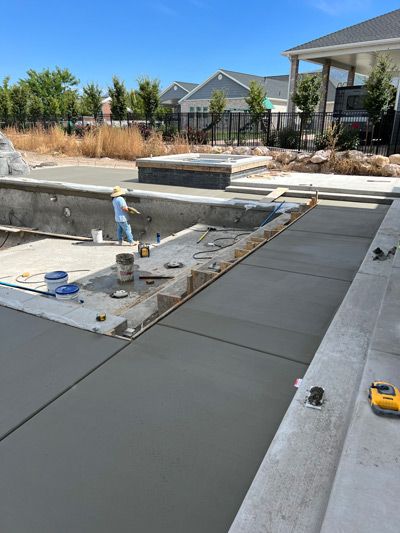 Concrete pool deck under construction with wet slabs, tools, and desert landscaping in the background