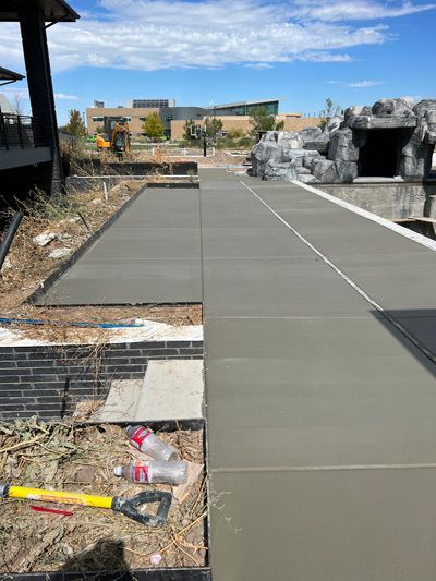 Partially built concrete walkway in a landscaped outdoor area with tools and debris nearby