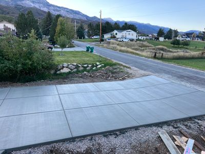Concrete driveway beside a rural road, with houses, trees, and mountains in the background.