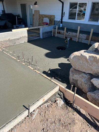 Outdoor patio under construction with fresh concrete slab, stone wall, and wooden forms.