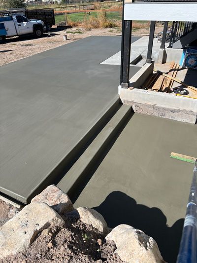 Concrete driveway beside a house with fresh gray slab and expansion joint near a porch foundation