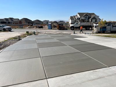 Concrete driveway under construction in a new suburban neighborhood, with houses and workers in the distance