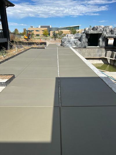 Walkway with concrete slabs leading past rocks and landscaping toward a building under a blue sky