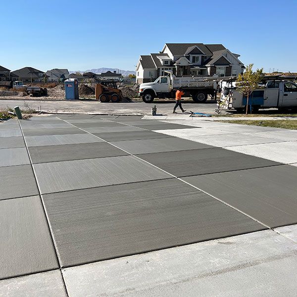 Freshly poured concrete driveway panels at a suburban house under construction, with workers and a truck nearby