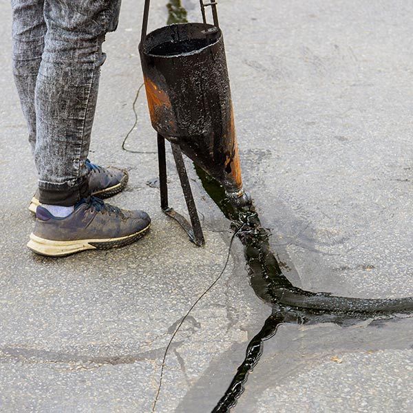Worker standing by a cut pipe leaking water onto cracked pavement