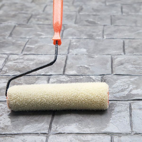 Paint roller with orange handle resting on gray brick paving