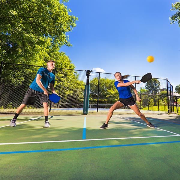 Two people playing pickleball on an outdoor court, one preparing a forehand under a bright blue sky.