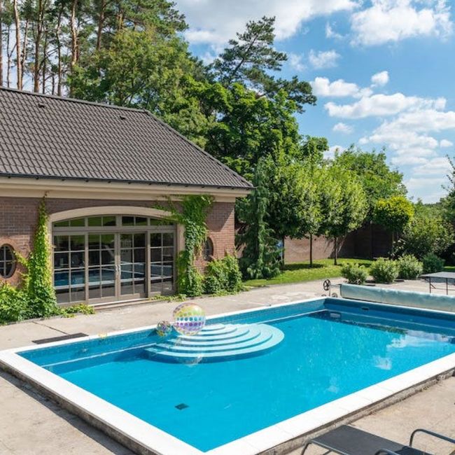 Backyard pool beside a house, with blue water and a colorful inflatable float under a sunny sky