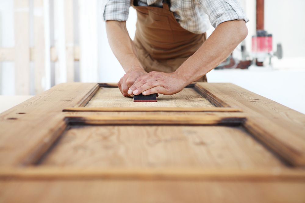 A Man Is Sanding A Piece Of Wood With A Sander — Roo’s Door & Window Maintenance In Sippy Downs, QLD