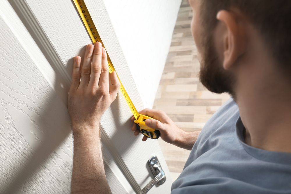 A Man Is Measuring A Door With A Tape Measure — Roo’s Door & Window Maintenance In Caloundra, QLD