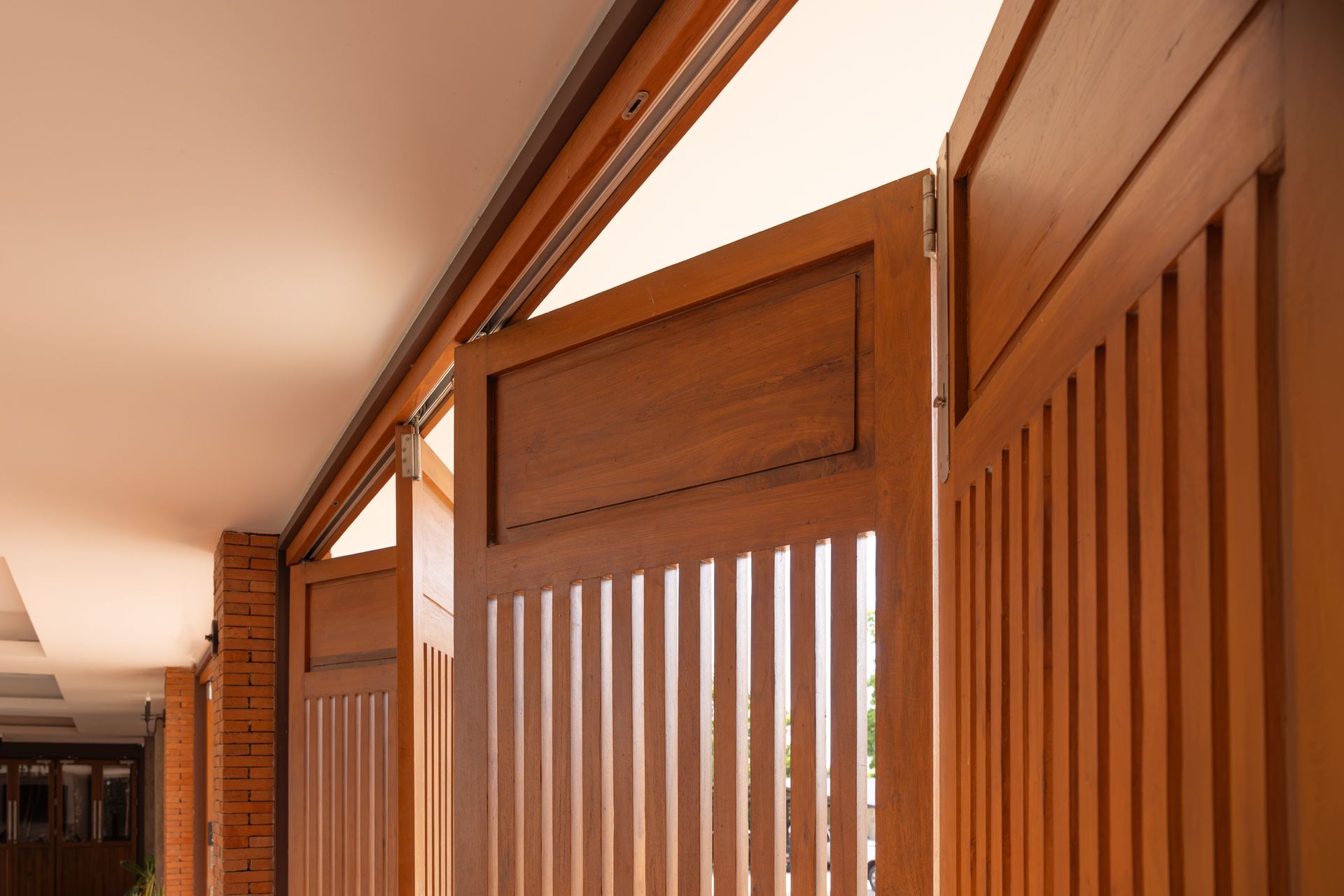Wooden Slatted Doors Along a Narrow Hallway With Warm Sunlight Streaming in — Roo’s Door & Window Maintenance In Sippy Downs, QLD