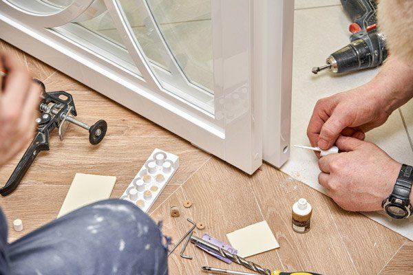 A Man Is Fixing A Door With A Drill On The Floor — Roo’s Door & Window Maintenance In Sippy Downs, QLD