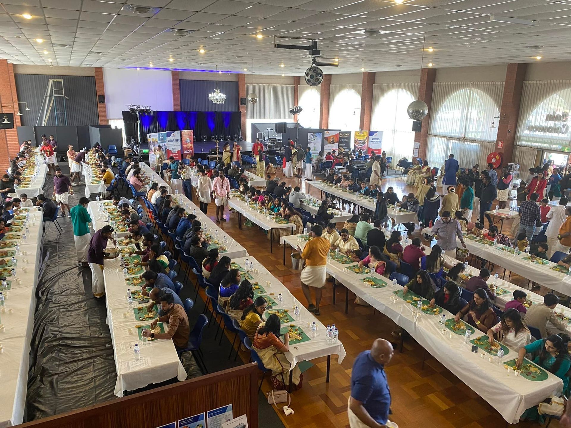 A large group of people are sitting at long tables in a large room. A large group of people are sitting at long tables in a large room.