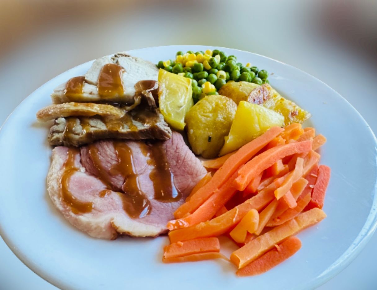 A white plate topped with meat potatoes carrots and peas