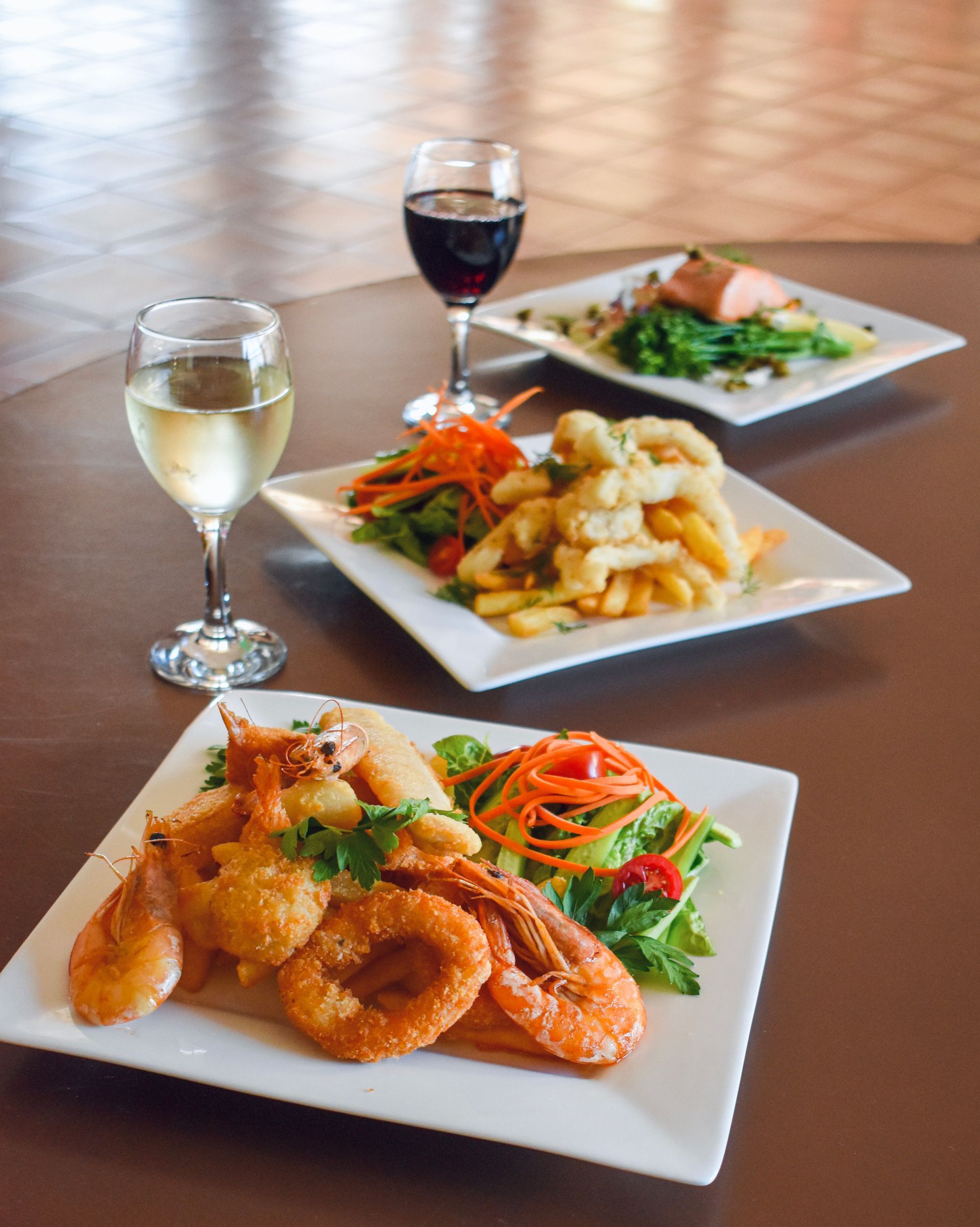 Three plates of food and a glass of wine on a table.