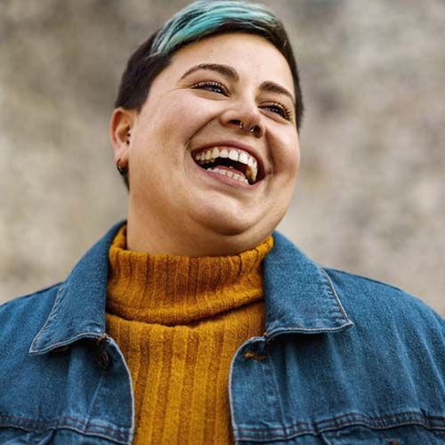 A young woman of non-binary sexuality smiles showing her teeth