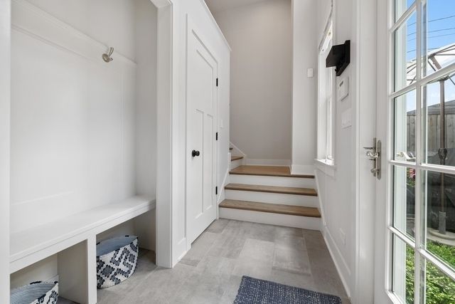 Entryway with white built-in bench and storage, leading to stairs and an exterior door with glass panes.