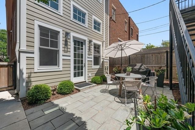 Backyard patio with gray pavers, white table, umbrella, and a light-colored house.