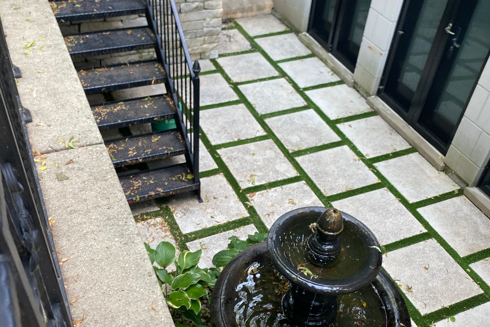 Exterior courtyard with fountain, stone pavers, green spaces, and stairs leading upwards.