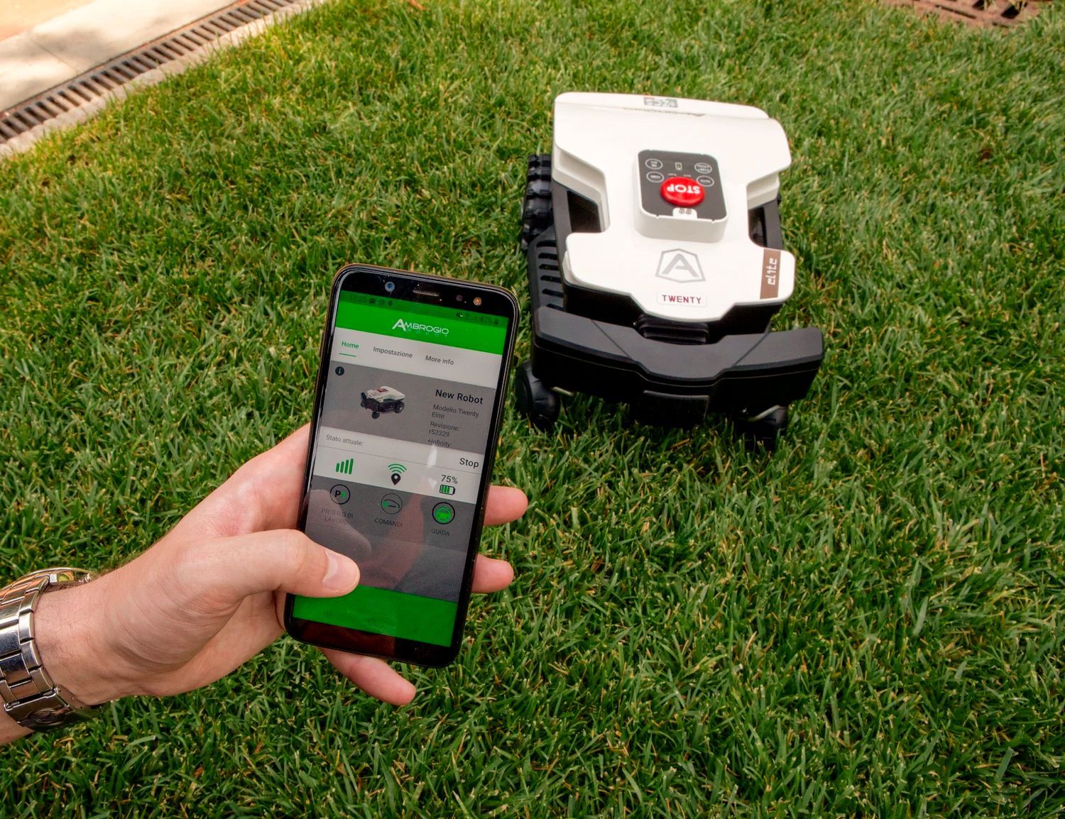 Person using smartphone to control a robotic lawnmower on a green lawn.