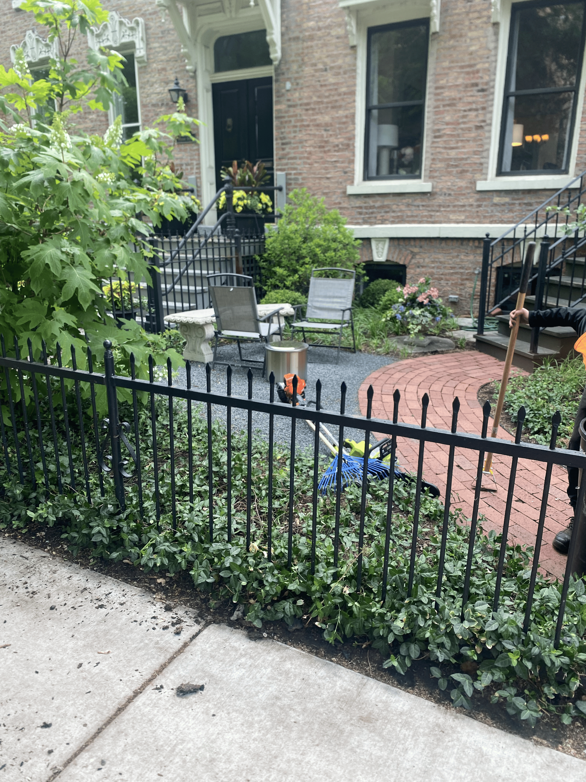 Black metal fence in front of a brick building's garden with chairs and plants.