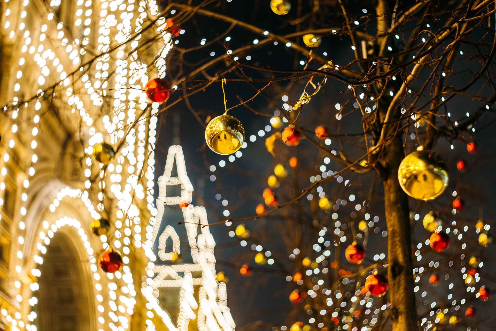 Holiday tree decorations with bright lights and ornaments in front of a building.