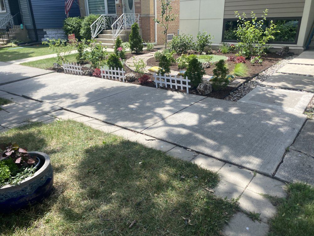 A house with a landscaped front yard, picket fence, and concrete walkway.