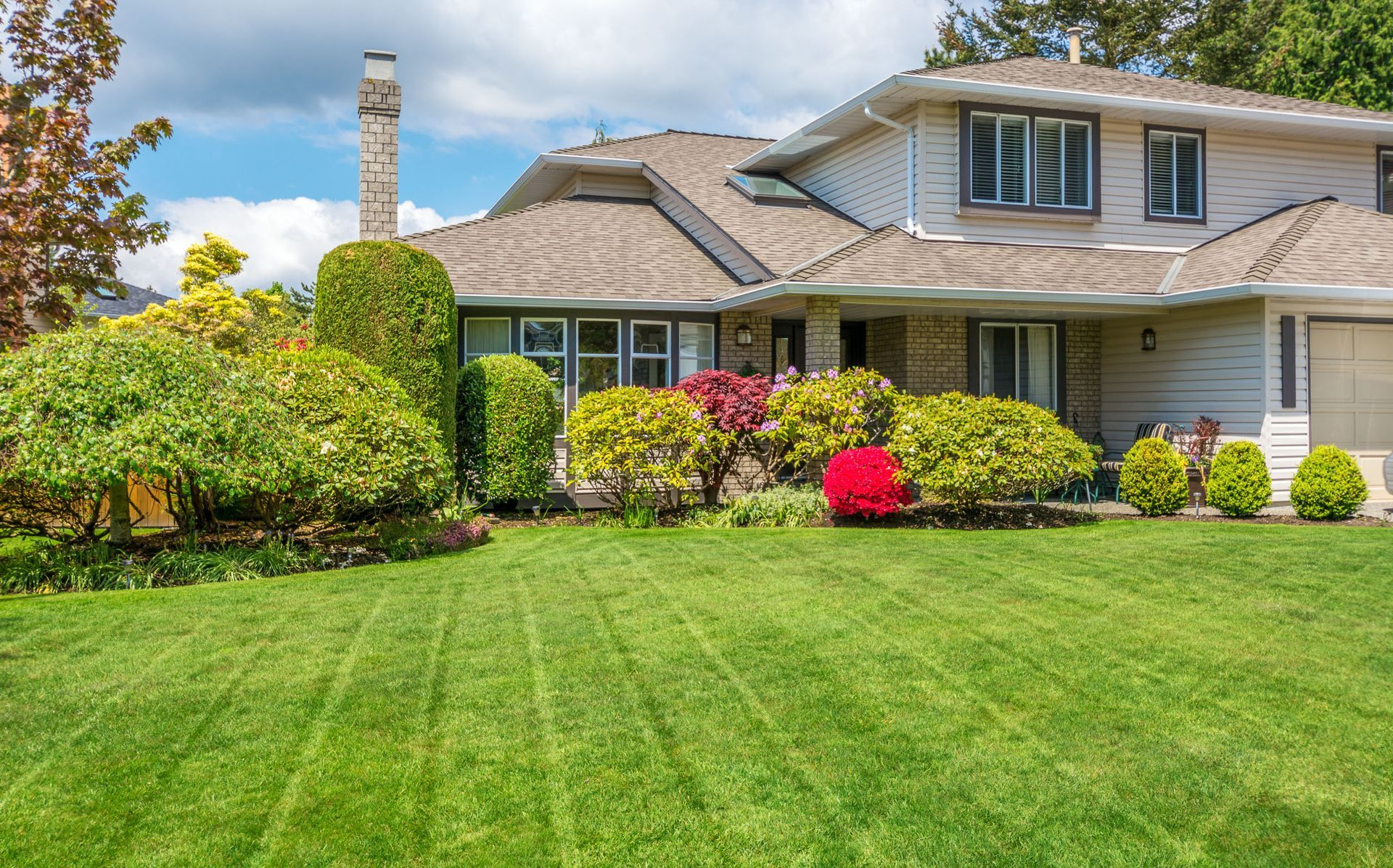 House with green lawn, landscaping, and a blue sky.