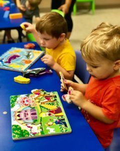Two young boys are playing with a puzzle on a blue table.