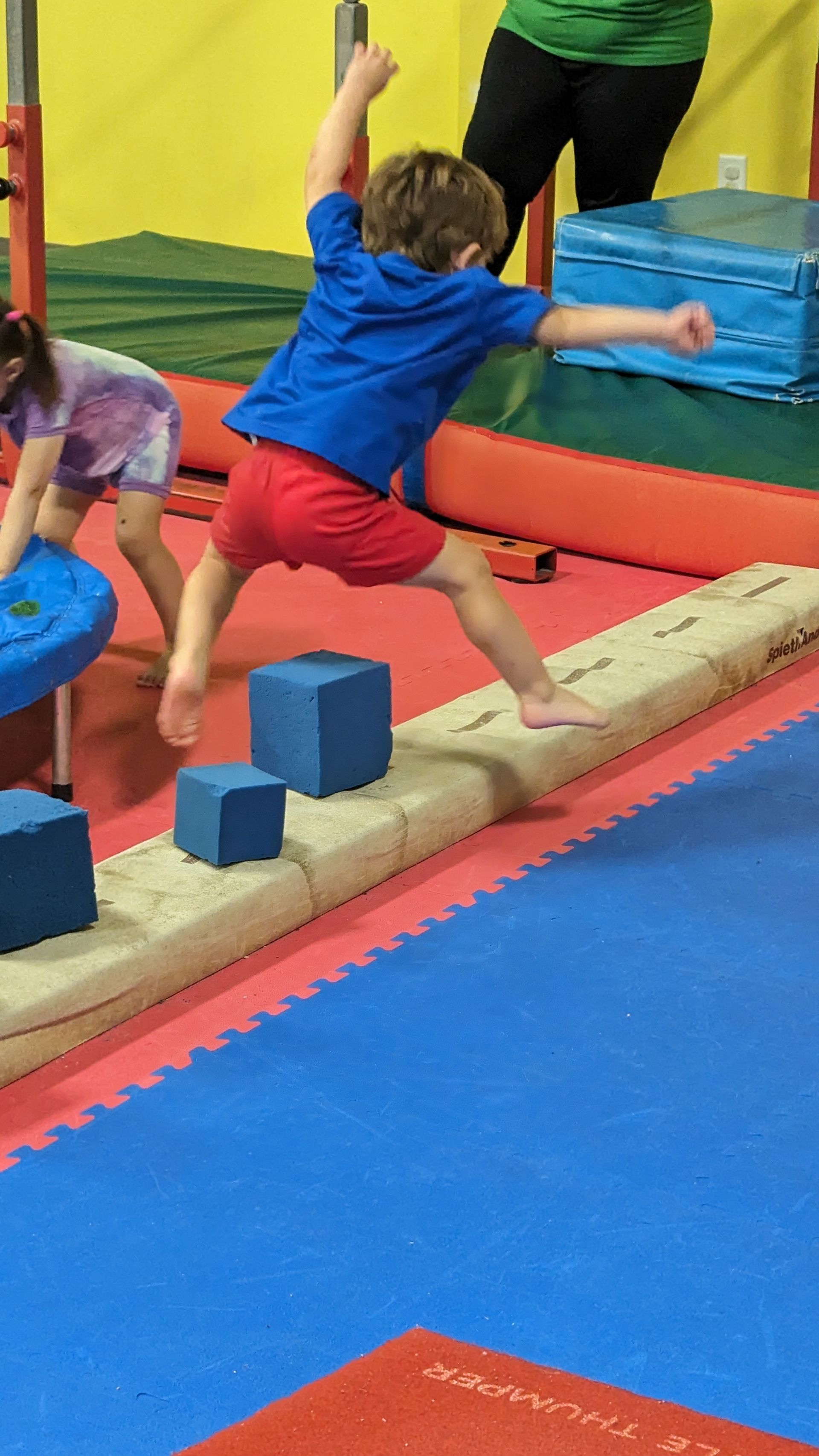 A young boy is jumping over a balance beam in a gym.