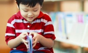 A young boy is sitting in a library reading a book.