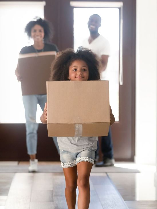 Family of three moving into a new home; child carrying a box.
