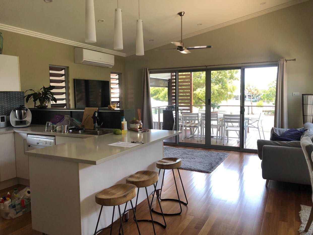 Modern kitchen and living room with island, stools, sofa, and sliding doors to a patio. — Schmucker Cleaning in Gulliver, QLD