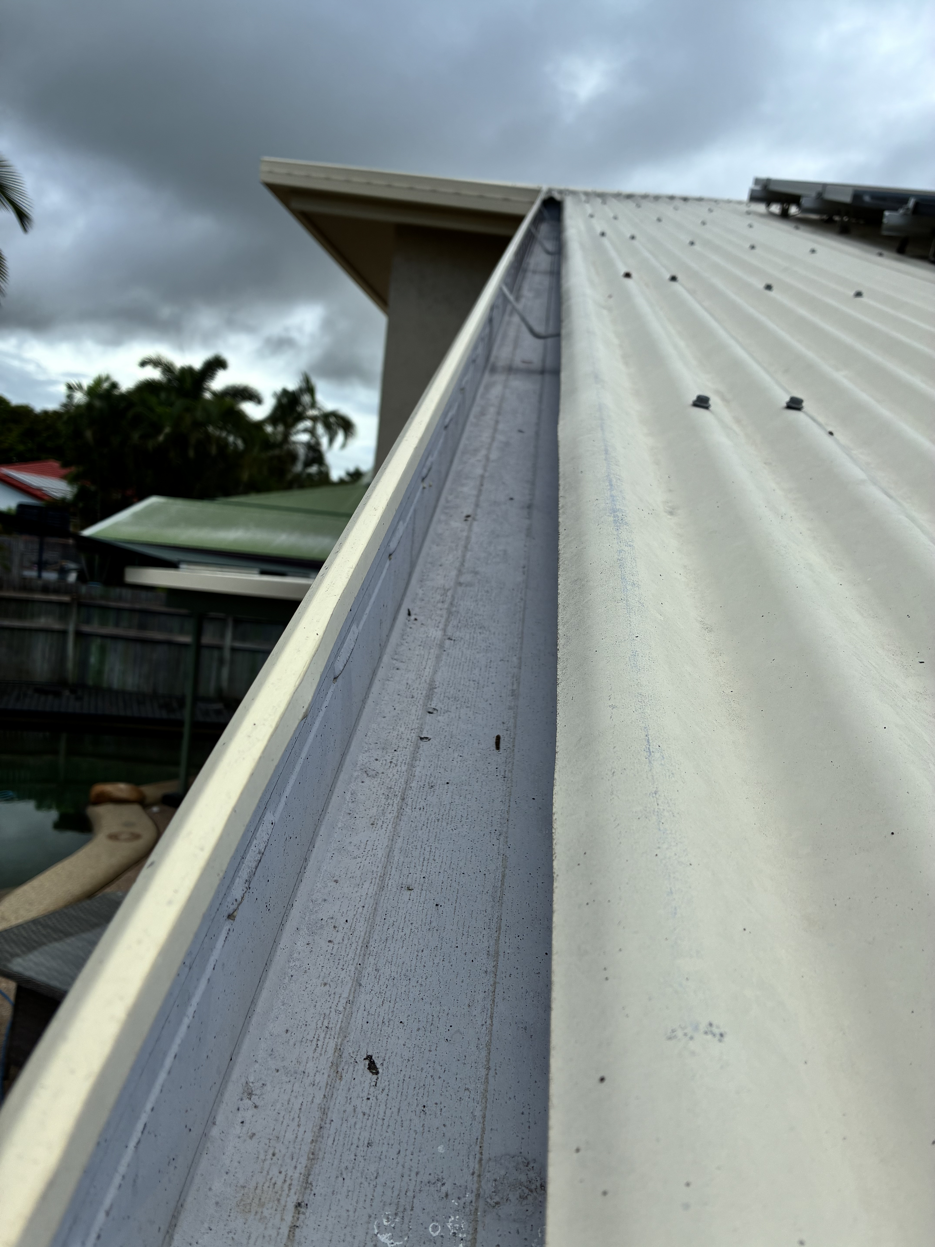 View Along a Metal Roof Gutter Leading to the Edge of a House Roof Against a Cloudy Sky — Schmucker Cleaning in Gulliver, QLD