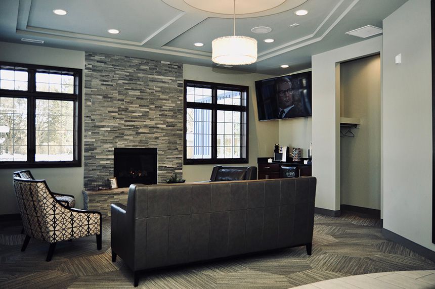 Modern office lounge with patterned chairs, dark sofa, windows, stone wall, and wall-mounted TV