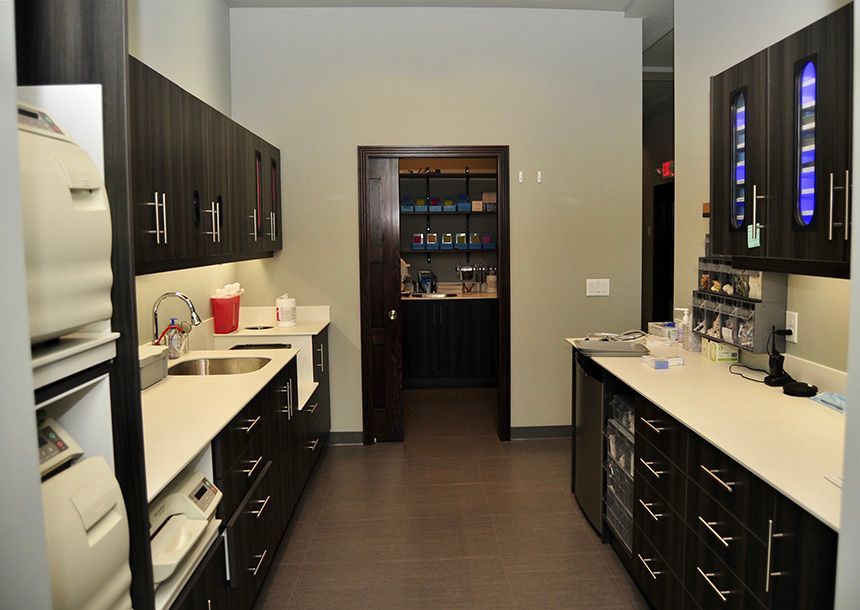 Modern kitchen with dark cabinets, white countertops, and stainless steel appliances, viewed down a narrow aisle